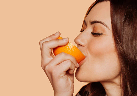 Woman eating orange slice, close-up on peach background, healthy eating concept