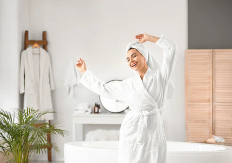 Happy woman in white bathrobe relaxing in modern bathroom with bathtub and houseplant