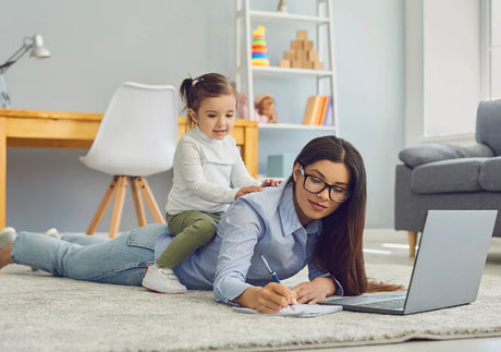 Mom working from home on laptop with child playing on her back in a cozy living room