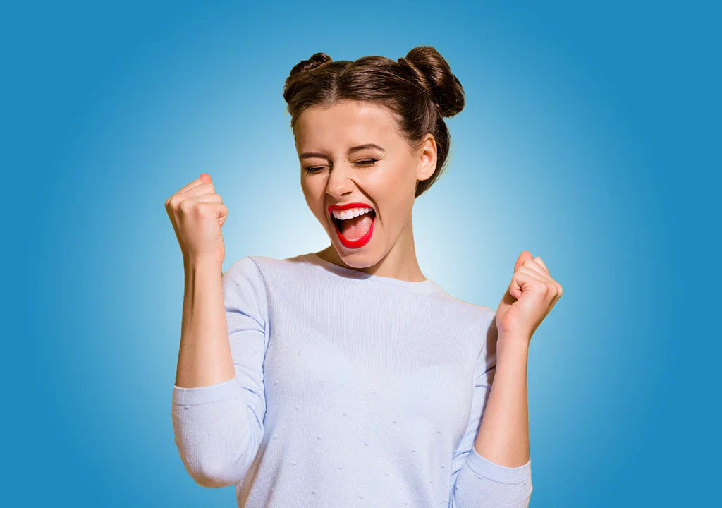 Excited young woman celebrating with clenched fists, blue background, success concept