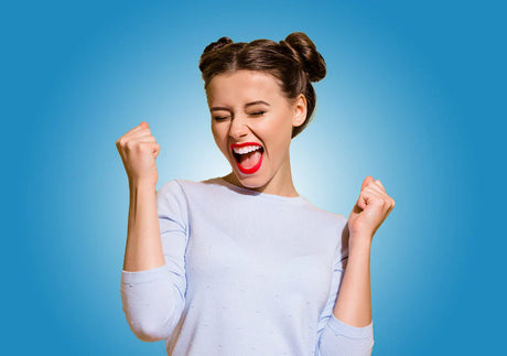 Excited young woman celebrating with clenched fists, blue background, success concept