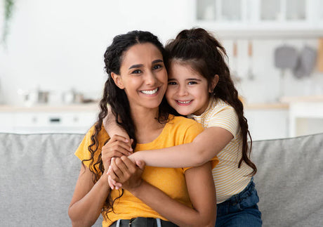 Smiling mother and daughter hugging on sofa in bright modern living room