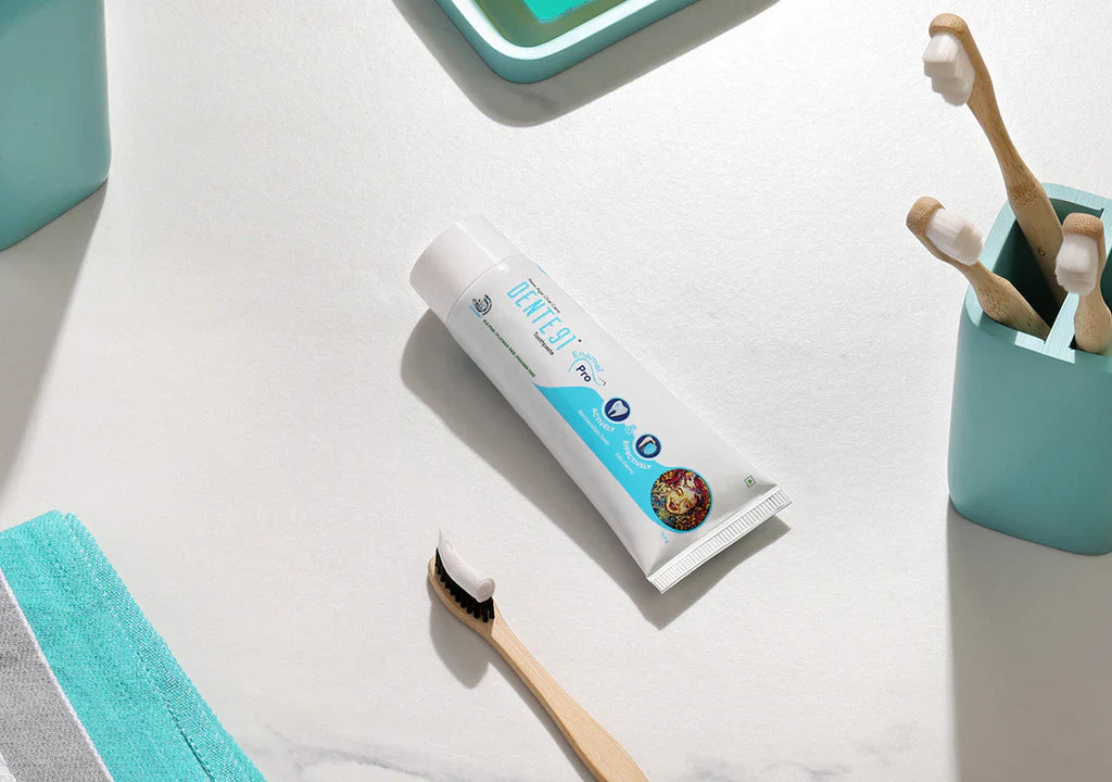 Mint toothpaste tube with bamboo toothbrushes and teal bathroom accessories on white counter