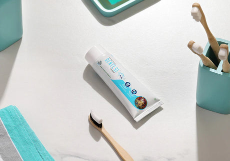Mint toothpaste tube with bamboo toothbrushes and teal bathroom accessories on white counter